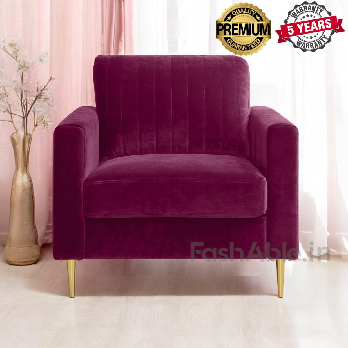 A plush maroon armchair with gold legs sits on a light floor beside a tall vase and pink curtains, inviting you to relax in style. Labeled Premium Quality Guaranteed and 5 Years Warranty, this Fashable chair is a must-buy for those who shop for elegance and durability.