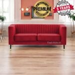 A red velvet sofa with vertical stitching is centered in a room with hardwood floors, featuring gold-tipped legs. Decorative wall lights accent the space. Overlaid text invites you to explore the Premium Quality Guaranteed badge and a 5 Years Warranty emblem.