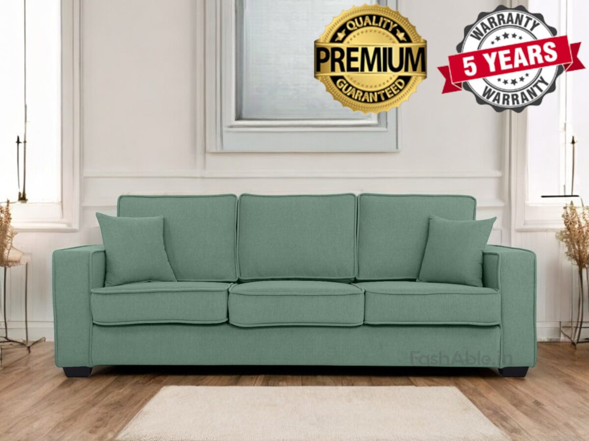 A green sofa with three large cushions and two smaller side cushions sits in a bright room with white walls, showcasing labels that read Premium Quality Guaranteed and 5 Years Warranty. Perfect for any fashable home decor, this piece transforms your living space into a stylish shop-like setting.